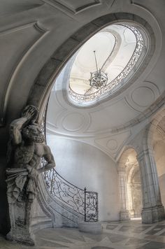 a statue in the middle of a room with a skylight above it and stairs leading to another area