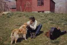 a woman sitting on the grass with her dog and another dog standing next to her