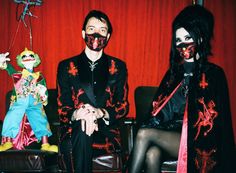 two people with painted faces sitting next to each other in front of a red curtain