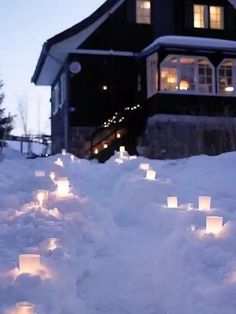 many lit candles are placed in the snow near a house at night with lights on