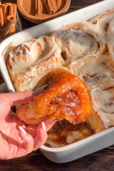 a person is taking a piece of cinnamon rolls out of a casserole dish