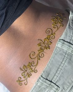 the back of a woman with gold tattoos on her lower body and side, showing an intricate design