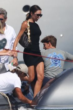 a woman in a short black dress is walking on the back of a boat with other people