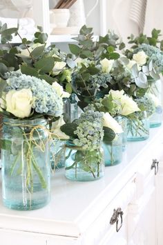 several mason jars filled with flowers and greenery