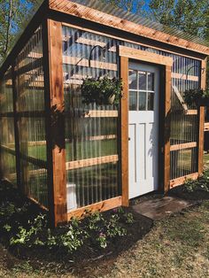 a small greenhouse with glass doors and plants growing in the ground next to it's door