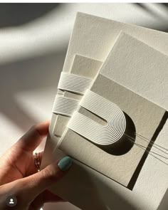 a person holding up some white paper with the letter e on it's side