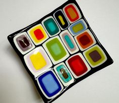 a colorful glass plate sitting on top of a white table next to a black frame