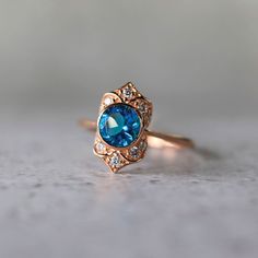 A vintage-inspired 6.5mm round gemstone bezel set 14K rose gold customizable engagement ring. Designed to inspire the vintage jewelry lover, romantic details make this wedding ring one of our most popular. We recommend setting this ring with a round ethically-made gemstone, a lab-created diamond or a moissanite gemstone. Starting at $1400, this setting is item CE-123987. A customizable engagement ring is a unique reflection of your love. Each element tells a story—choose from a beautiful array o Blue Stone Signet Ring, Swiss Blue Topaz Engagement Ring, Swiss Blue Topaz Ring, Blue Topaz Engagement Ring, Style Art Deco, Blue Topaz Gemstone, Topaz Engagement Ring, Swiss Blue Topaz, Jewelry For Her