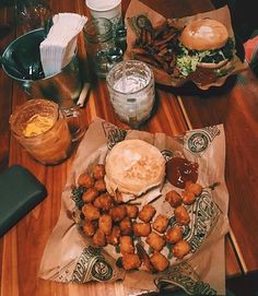 a wooden table topped with lots of food on top of paper wrappers and glasses