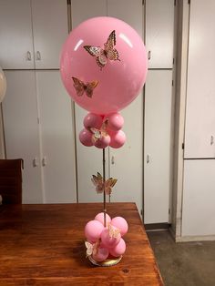 a pink balloon with butterflies on it sitting on top of a wooden table next to a vase