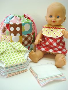 a baby doll sitting next to some cloths and a bag with a bib on it