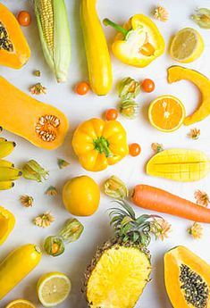 various fruits and vegetables laid out on a white surface with oranges, lemons, tomatoes, pineapple, cornucons, carrots