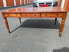 an old wooden desk sitting in the middle of a parking lot next to a car