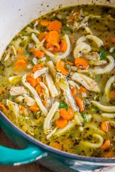 chicken noodle soup with carrots and parsley in a blue pot