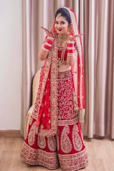 a woman in a red and gold bridal outfit posing for the camera with her hands up to her face