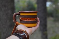 a hand holding a yellow and brown coffee cup with leather straps on it's wrist