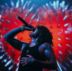 a man with long hair holding a microphone up to his ear while standing in front of a red background