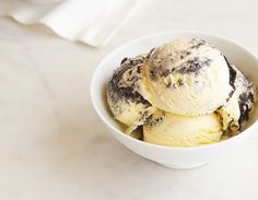 three scoops of ice cream in a white bowl on a marble countertop next to a napkin