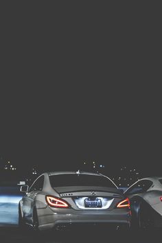 two cars parked next to each other in front of a dark sky with lights on