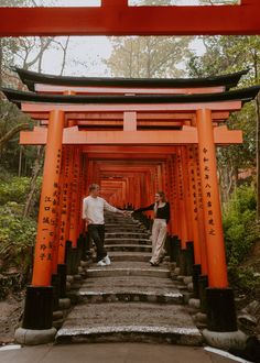 two people standing in front of an orange tori tori gate with steps leading up to them