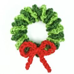 a crochet christmas wreath with red and green yarn tied around it, on a white background