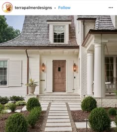 a white house with steps leading up to the front door and entry way that is surrounded by bushes