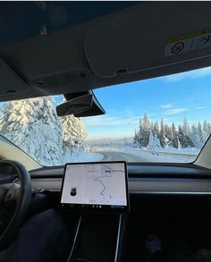 the dashboard of a car with a tablet on it in front of snow covered trees