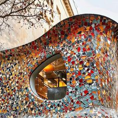 an unusual building with colorful tiles on it's side and a tree in the foreground