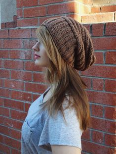 a woman standing next to a brick wall wearing a knitted hat with braids