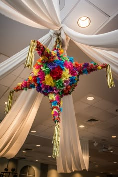 a colorful star hanging from the ceiling with white drapes and streamers around it