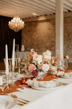 the table is set with white and orange flowers, silverware, candles and napkins