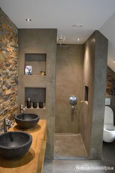 two black bowls are on the counter in this modern bathroom with stone walls and flooring