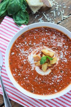 a white bowl filled with tomato soup and garnished with parmesan cheese