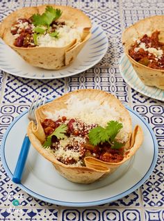 three tacos with meat, rice and cilantro on a blue and white tablecloth