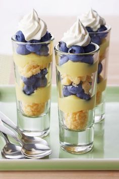 three desserts with blueberries and whipped cream in glasses on a green serving tray