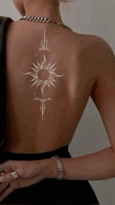 the back of a woman's body with an intricate sun tattoo on her left shoulder