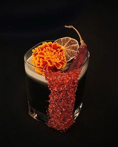 the drink is garnished with orange and red flowers on the black tablecloth