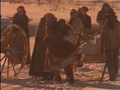 several people standing around in the snow with an old fashioned wagon and spinning wheel behind them