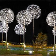 three metal sculptures with lights on them in the grass at night, and one is lit up