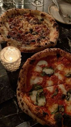 two pizzas sitting on top of a table next to a candle and some glasses