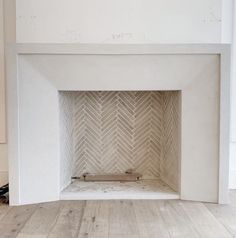 an empty room with a white fireplace and wood floors