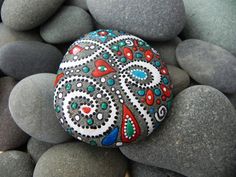 a painted rock sitting on top of some rocks covered in gravel and stones with colorful designs