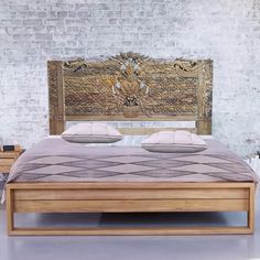 a wooden bed with two pillows on it in front of a brick wall and floor