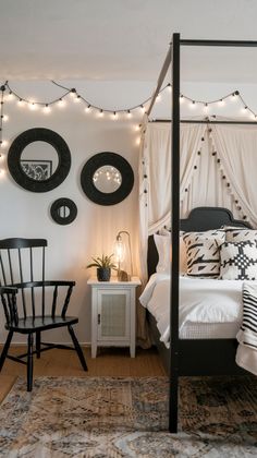 a bedroom with white walls and lights strung from the ceiling, black bed frame, round mirrors on the wall