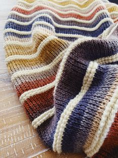 a multicolored knitted blanket laying on top of a wooden floor