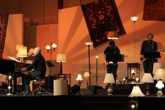 a group of people that are standing in front of a piano and some lamps on a stage