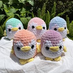 four small crocheted birds sitting on top of a white cloth next to green plants