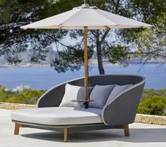 an outdoor chaise lounge chair with an umbrella on the top and water in the background