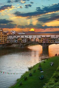 the sun is setting over a river with buildings on both sides and a bridge in the distance