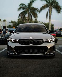 the front end of a silver car parked in a parking lot next to palm trees